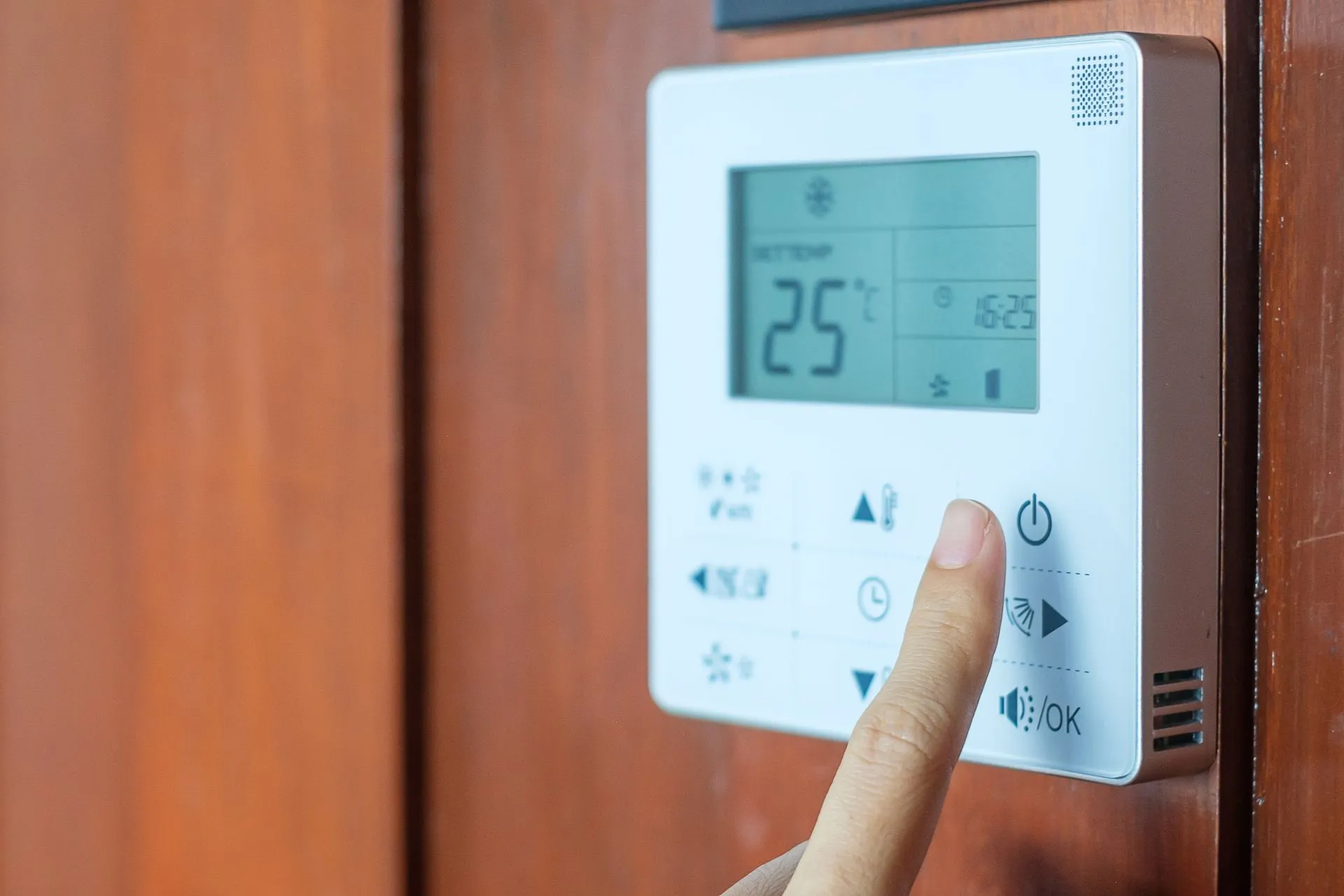Homeowner controlling a wall-mounted smart thermostat with a smartphone.
