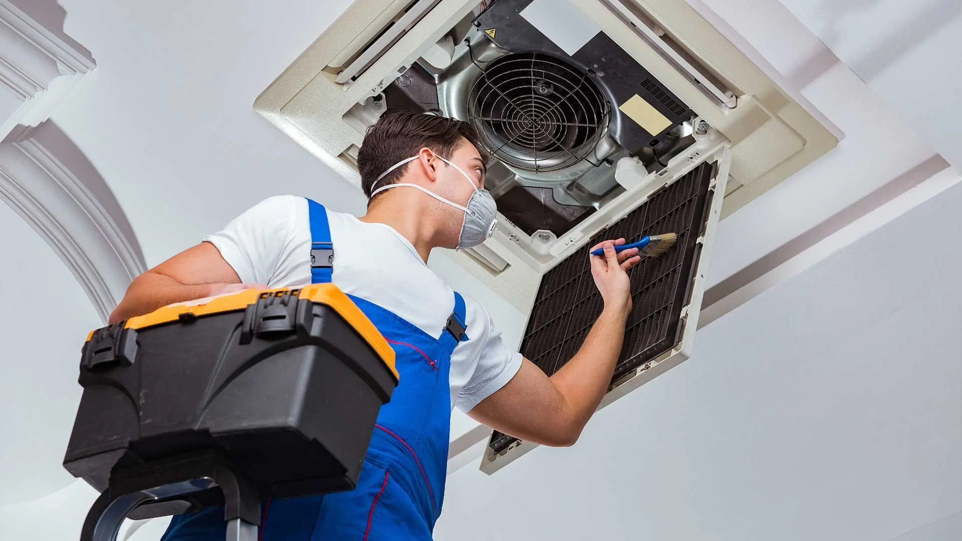 A man wearing a mask is working on an air duct cleaning services.