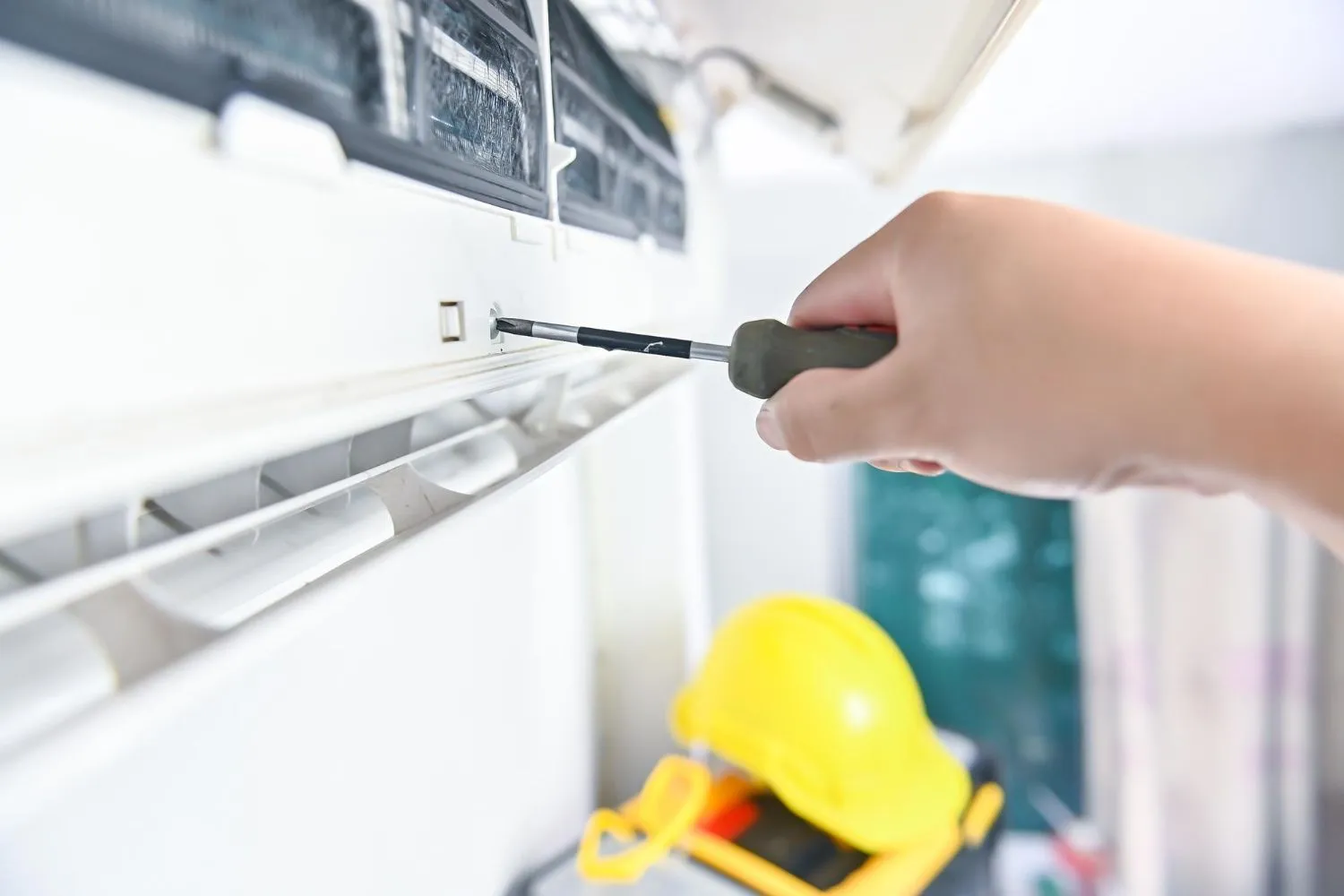 A technician from Reid Heating & Air is fixing an air conditioner with a screwdriver.